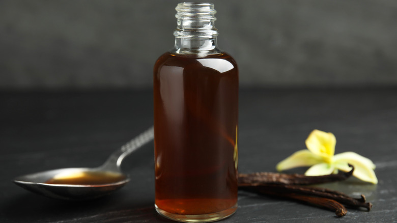 vanilla extract in bottle and spoon with vanilla sticks and flower