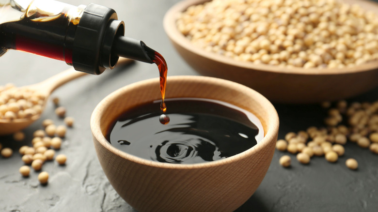 bottle pouring soy sauce into small bowl, with loose soybeans in background