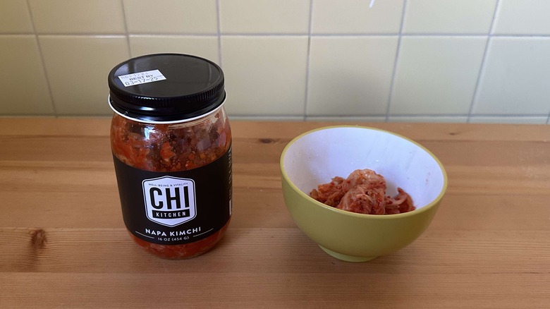 Container of Chi Kitchen Napa kimchi next to bowl of kimchi on table