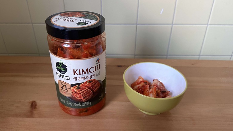 Bibigo kimchi jar next to bowl of kimchi on table