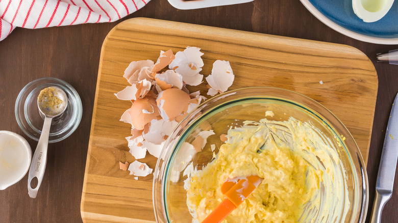 Deviled egg filling in bowl on board with egg shells