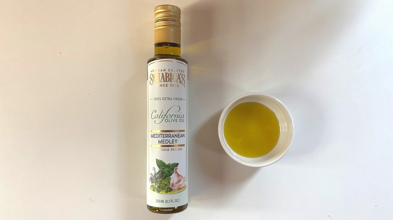 Bottle of Sciabica's Mediterranean Medley olive oil next to white dish of oil on white table