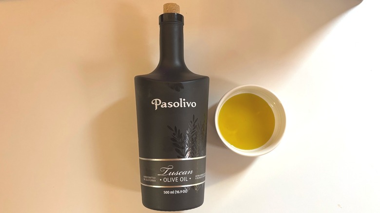 Bottle of Pasolivo olive oil next to small white bowl of oil on white table