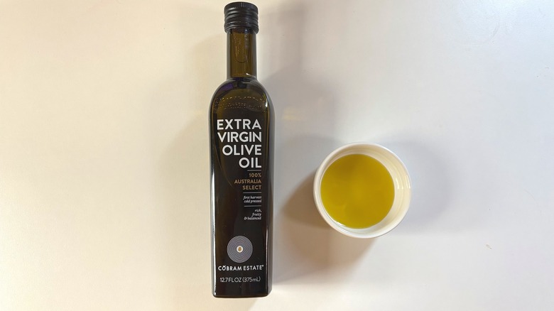 Bottle of Cobram Estate olive oil next to white dish of oil on white table