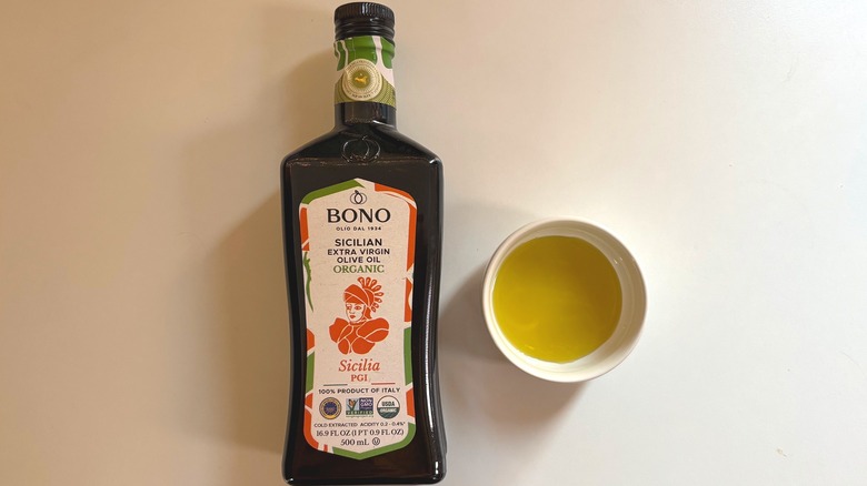 Bottle of Bono Sicilia PGI olive oil next to white dish of oil on white table