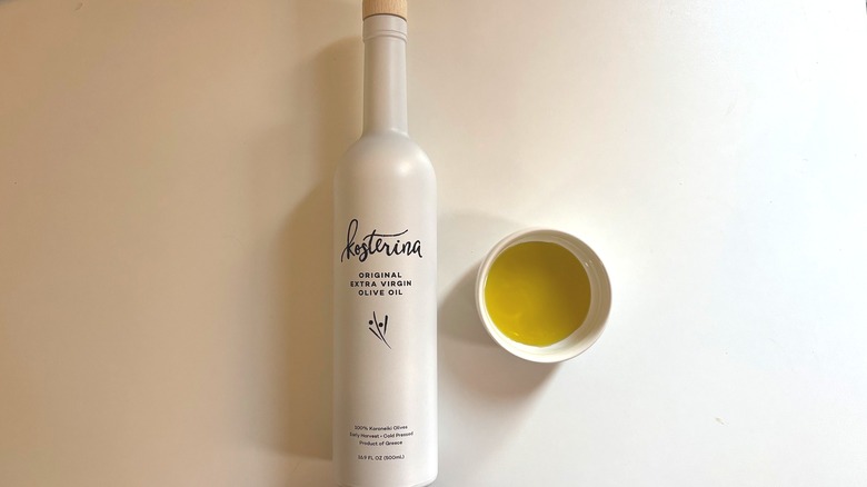 White bottle of Kosterina olive oil next to white dish of oil on white table