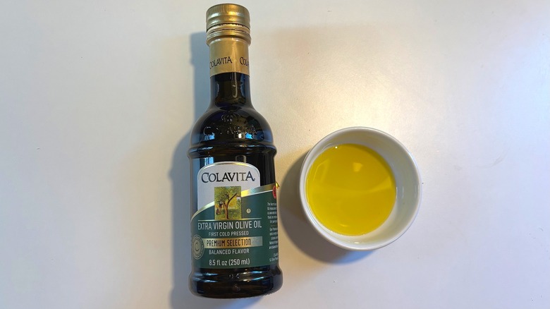 Bottle of Colavita olive oil next to white dish of oil on white table