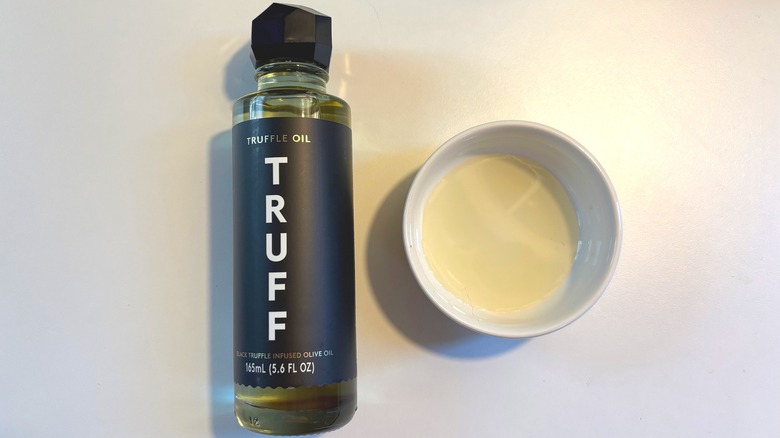 Bottle of TRUFF truffle-infused olive oil next to white dish of oil on white table