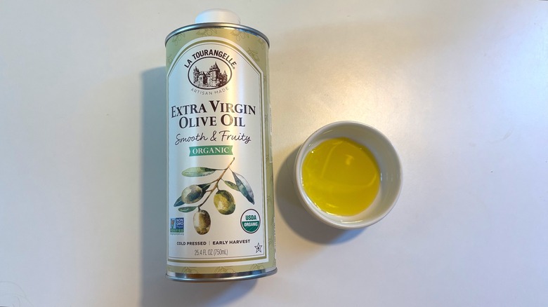 Bottle of La Tourangelle olive oil next to small white bowl of oil on white table