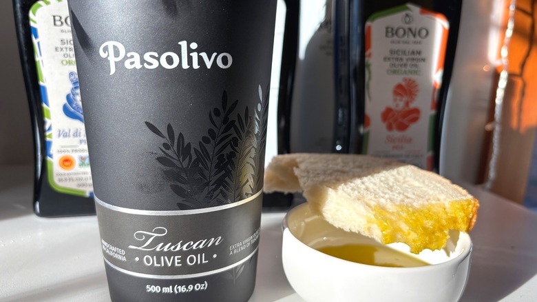 Bottle of Pasolivo olive oil next to slice of bread dipped in oil on white table