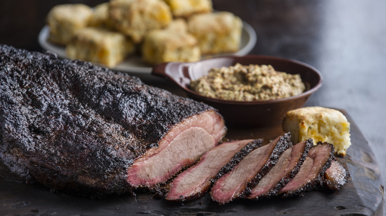 sliced brisket on a wooden cutting board next to squares of corn bread