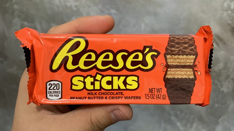 A hand holding up a package of Reese's Sticks