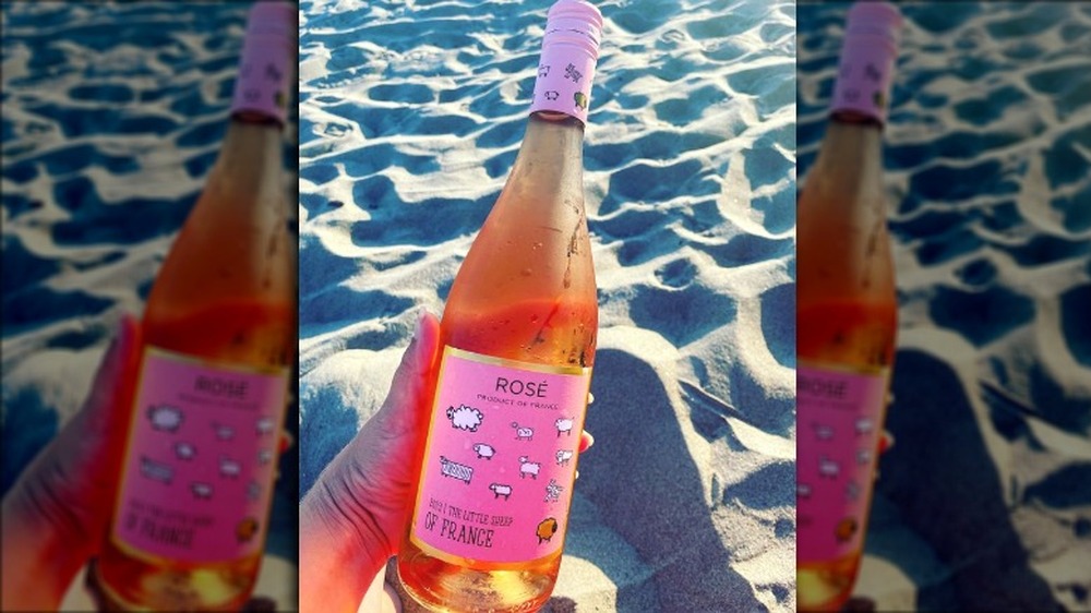 Hand holding a bottle of rose wine on the beach