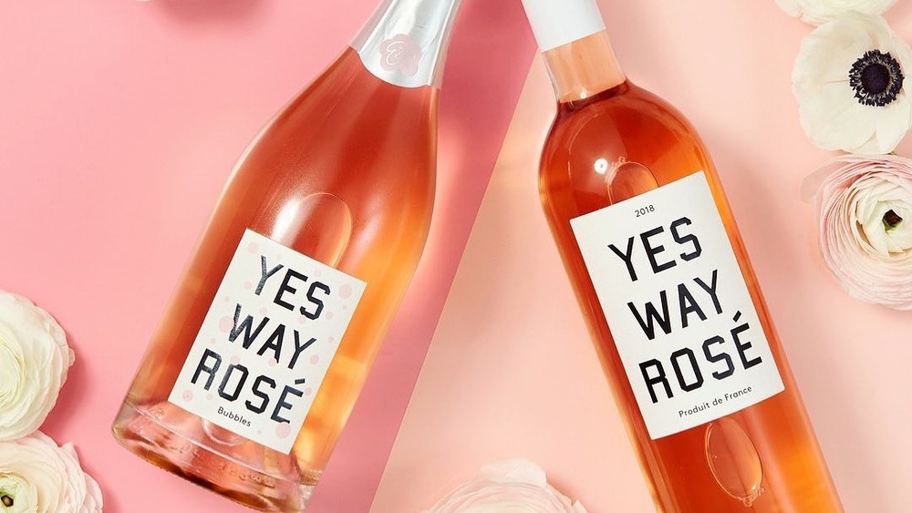 Two bottles of Yes Way Rosé on a pink surface with flowers