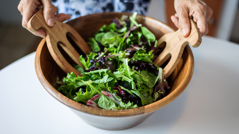 tossing mixed greens in a wooden bowl