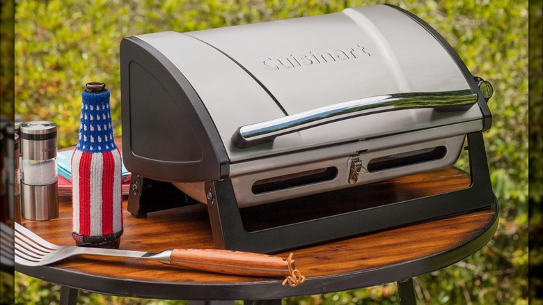 Cuisinart Grillster Portable Gas Grill with Locking Lid on wooden table alongside grilling accessories