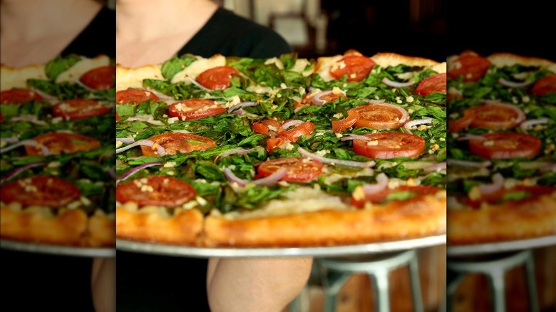 Person carrying a basil and tomato pizza 