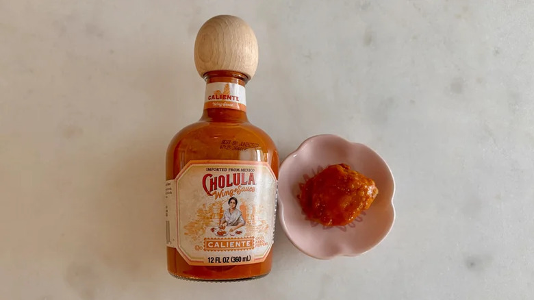 A bottle of Cholula caliente wing sauce on a counter next to a small bowl of sauce