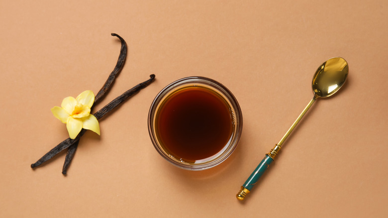 Vanilla extract surrounded by a spoon and some vanilla pods and a flower