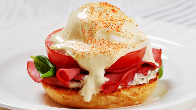 Egg benedict with a poached egg, tomato, basil and ham on an English muffin, topped with mock Hollandaise sauce