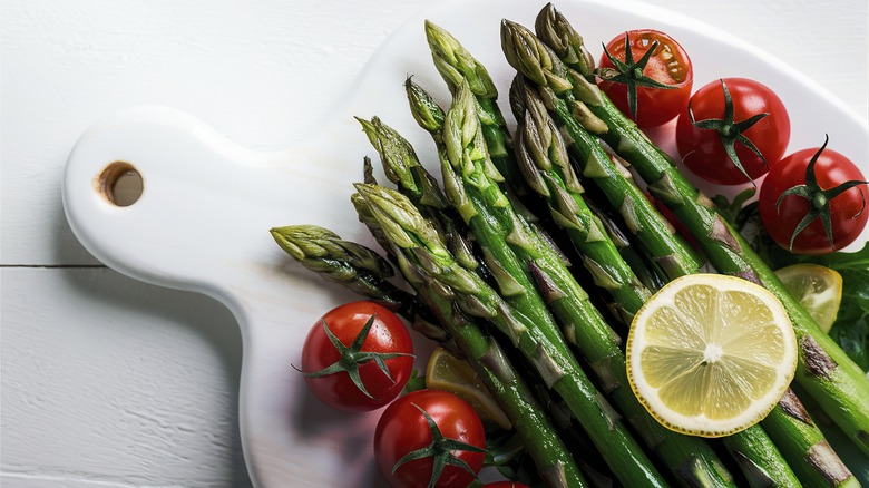 cooked asparagus on a cutting board with tomatoes