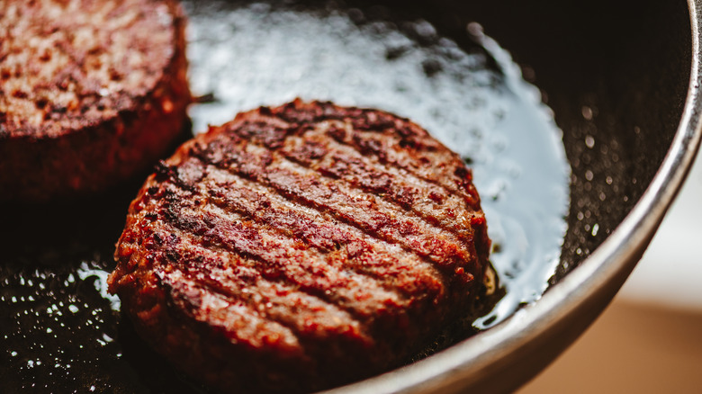 A cooked burger patty searing in a pan