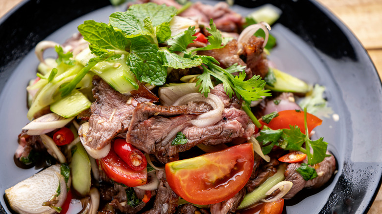 Thai grilled beef salad on a black plate.