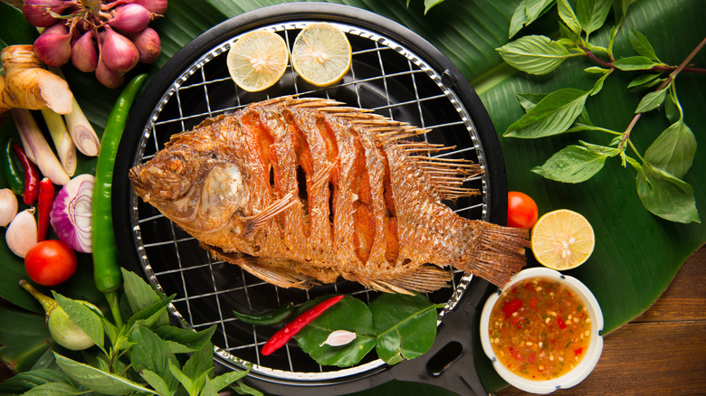 Fried fish on a metal grate with dipping sauce and ingredients