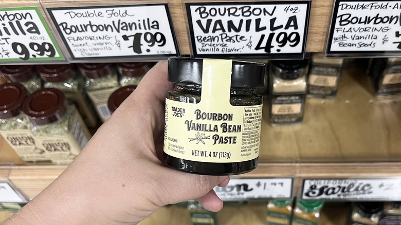 Hand holding Trader Joe's vanilla bean paste jar in store aisle