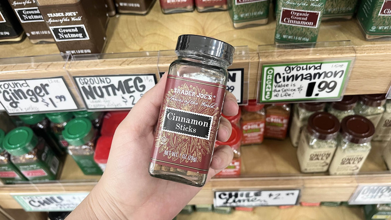 Hand holding Trader Joe's cinnamon sticks bottle in store aisle