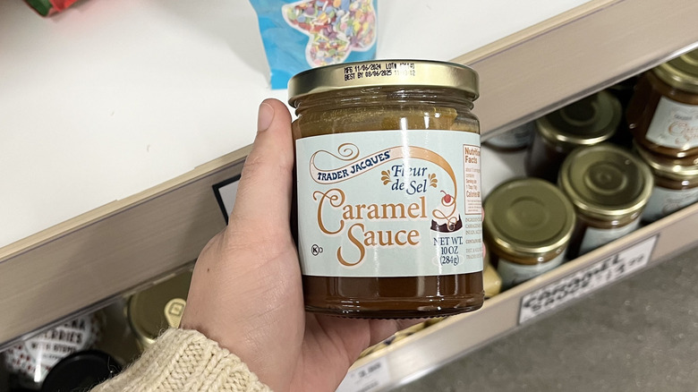 Hand holding Trader Joe's caramel sauce jar in store aisle