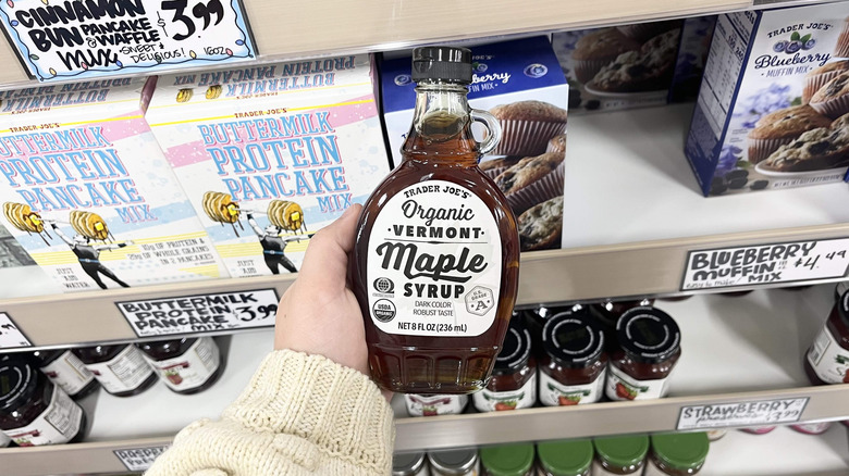 Hand holding Trader Joe's maple syrup bottle in store aisle