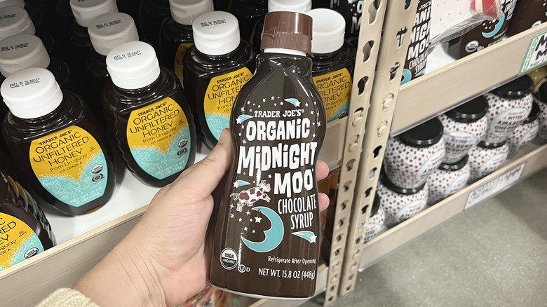 Hand holding Trader Joe's chocolate sauce bottle in store aisle