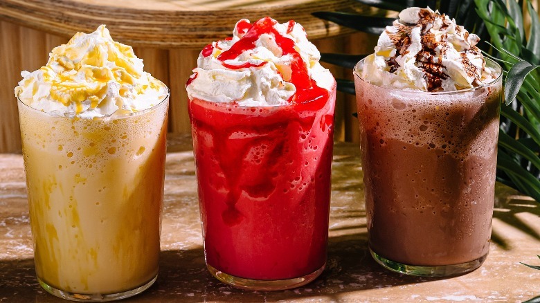 Chocolate, strawberry, and pineapple milkshakes lined up on a shelf