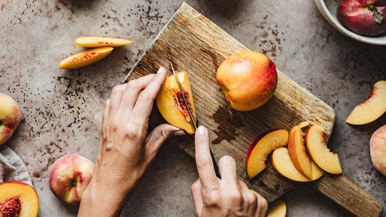 Hands slicing freestone peaches on cutting board