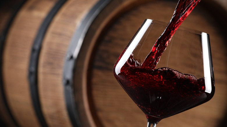 red wine poured in front of barrel