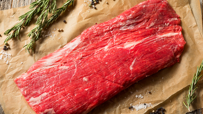 Raw flank steak with rosemary on parchment paper