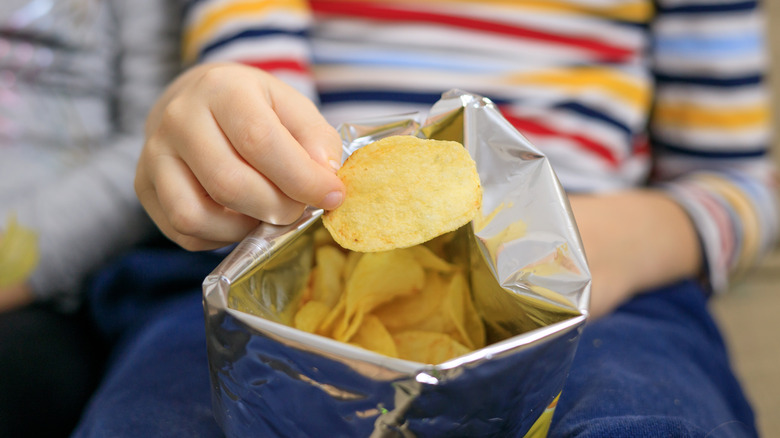 hand holding chip from bag of chips