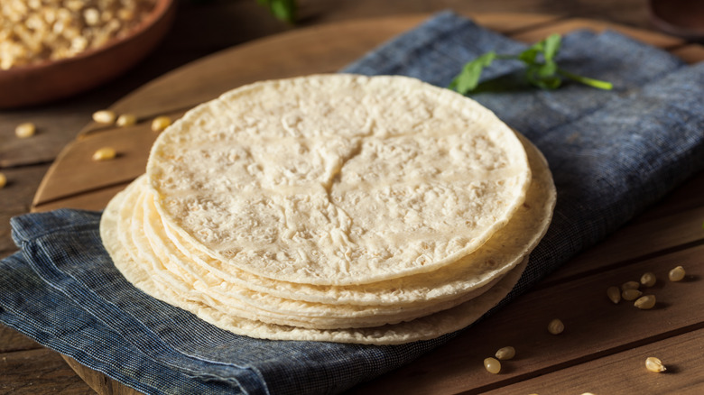 A stack of tortillas rest on a towel placed on a wooden table