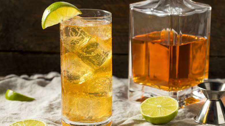 A whiskey ginger highball next to bottle of whiskey and limes