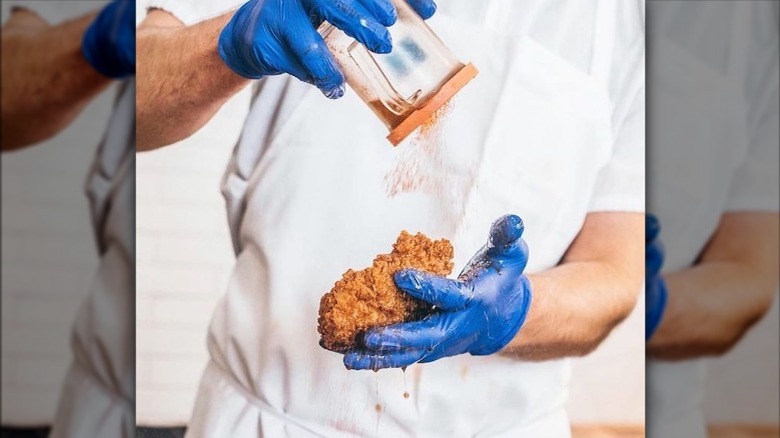 adding spice to piece of fried chicken