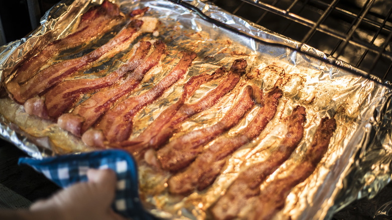 Hand removing bacon from an oven 