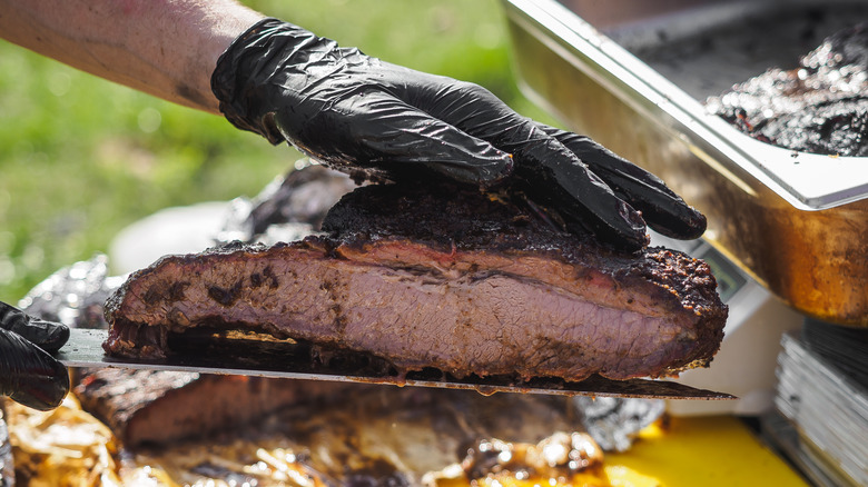 Gloved hands lift a smoked brisket off a cutting board