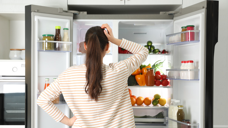 person scratching head while looking into fridge