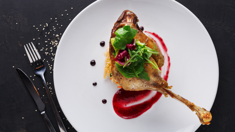 A leg of duck confit with purple sauce and green herbs