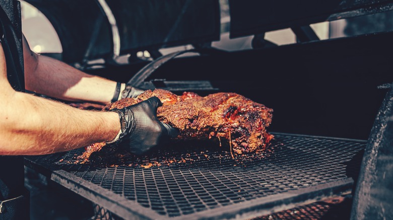 gloved hands moving pork shoulder on smoker