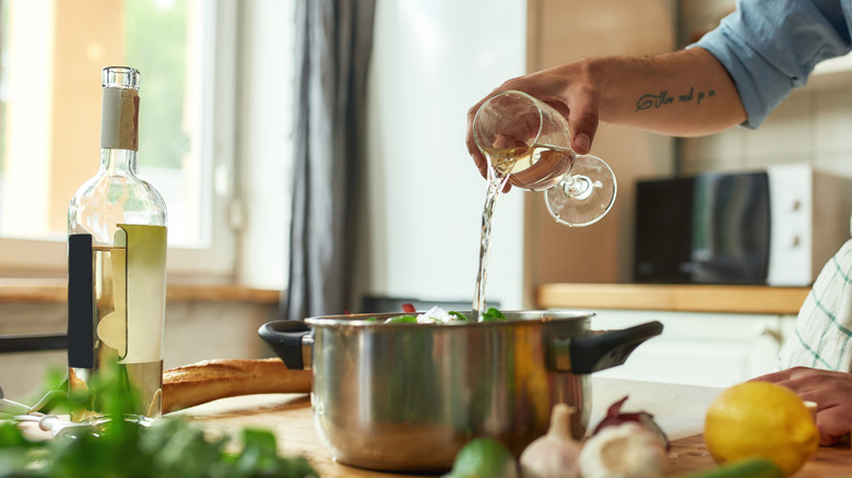 cook pouring white wine into a pot on the counter