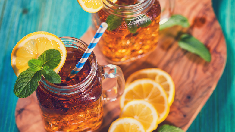 Two cold mason jars filled with sweet tea on a wooden board.