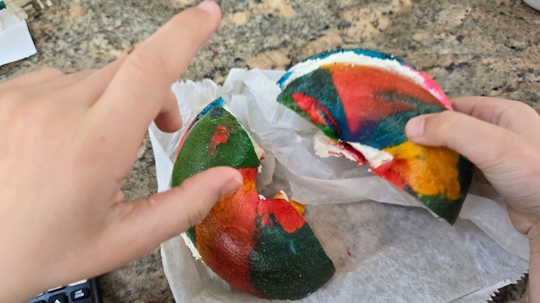 Hands unwrapping a rainbow bagel