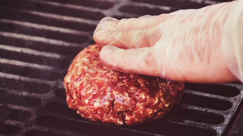Burger on a grill with a hand